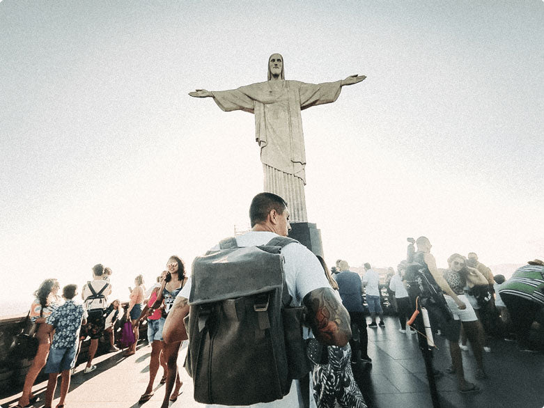 A low shot of a man wearing a backpack in front of Christ the Redeemer Statue in Brazil